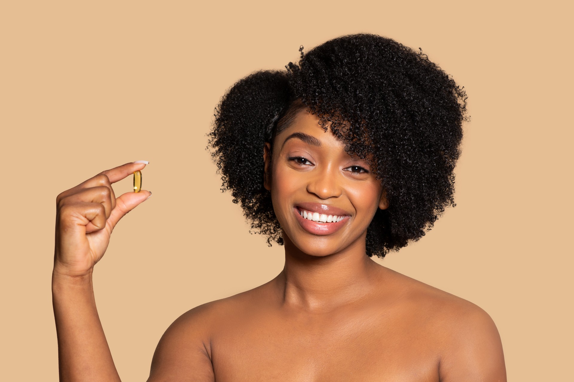 Mujer negra feliz sosteniendo suplemento, cabello rizado, fondo beige